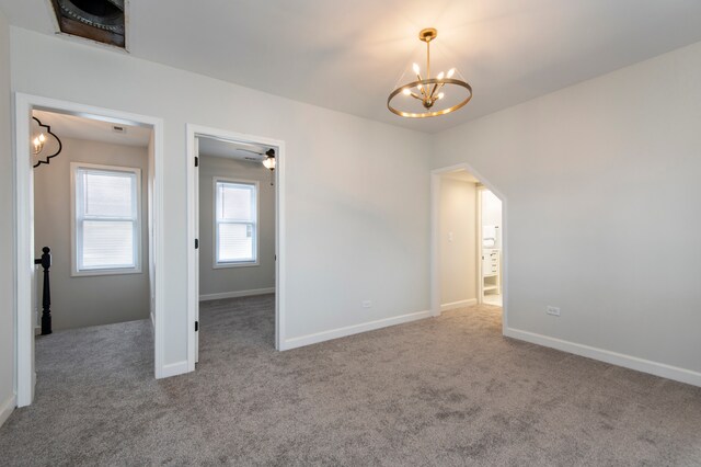 carpeted spare room featuring ceiling fan with notable chandelier