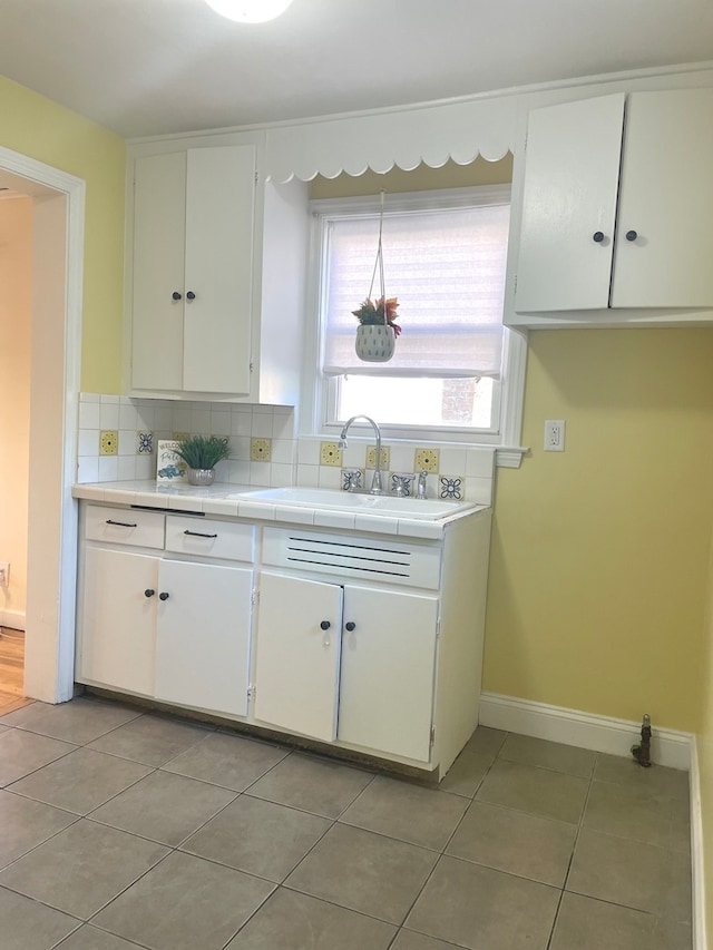 kitchen featuring backsplash, light tile patterned flooring, white cabinetry, and sink