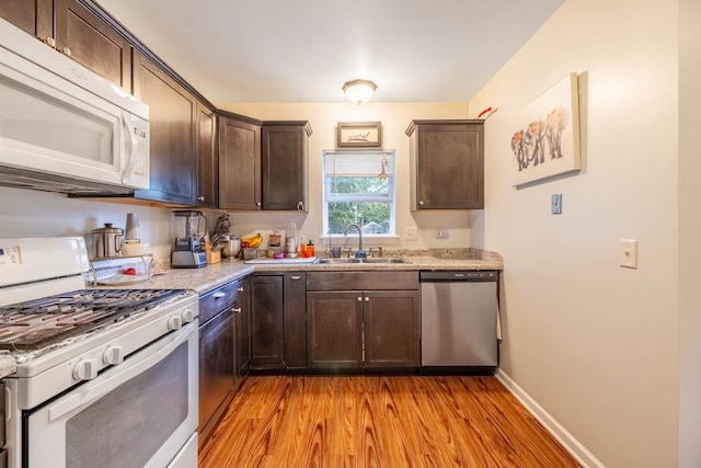 kitchen featuring white appliances, sink, light hardwood / wood-style flooring, dark brown cabinets, and light stone counters