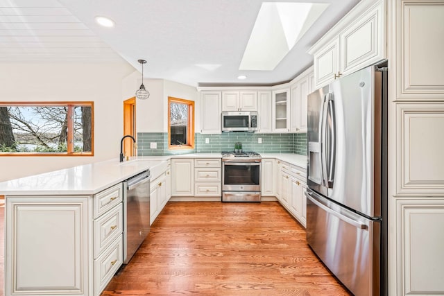 kitchen with a skylight, hanging light fixtures, kitchen peninsula, light hardwood / wood-style floors, and appliances with stainless steel finishes