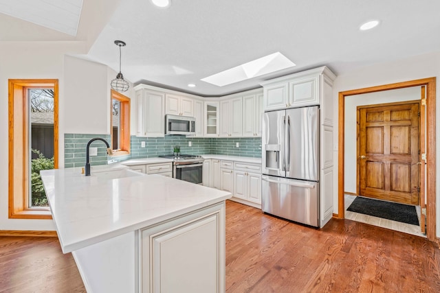 kitchen with white cabinetry, sink, stainless steel appliances, pendant lighting, and light hardwood / wood-style floors