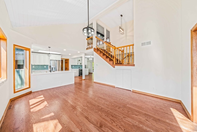 unfurnished living room featuring sink, high vaulted ceiling, and light hardwood / wood-style floors