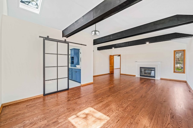 unfurnished living room with beam ceiling, a barn door, and wood-type flooring