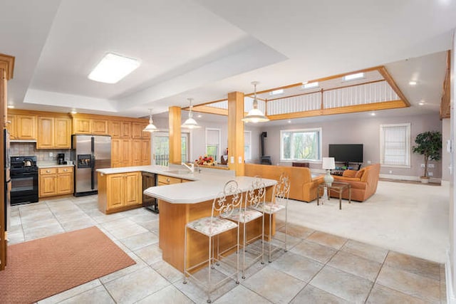 kitchen featuring kitchen peninsula, a kitchen breakfast bar, a raised ceiling, and black appliances