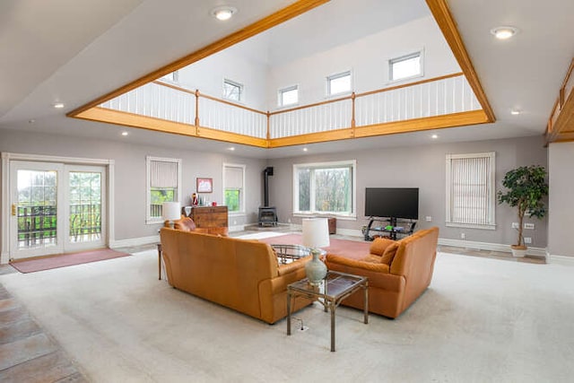 carpeted living room featuring a towering ceiling, a wood stove, and plenty of natural light