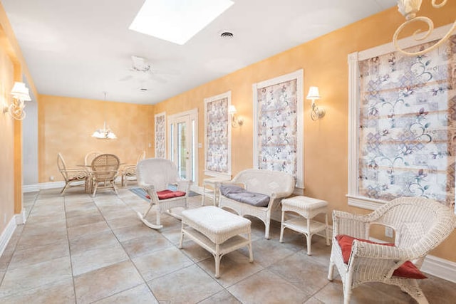 living area featuring a skylight, light tile patterned floors, and ceiling fan with notable chandelier