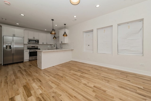 kitchen featuring pendant lighting, white cabinets, light hardwood / wood-style flooring, appliances with stainless steel finishes, and kitchen peninsula