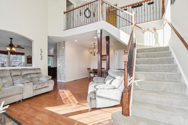 living room with a towering ceiling, ceiling fan with notable chandelier, and hardwood / wood-style flooring