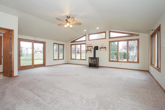 unfurnished living room with light colored carpet, a wood stove, a wealth of natural light, and vaulted ceiling