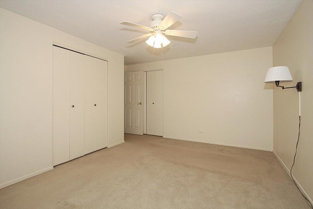 unfurnished bedroom with ceiling fan, light carpet, and two closets