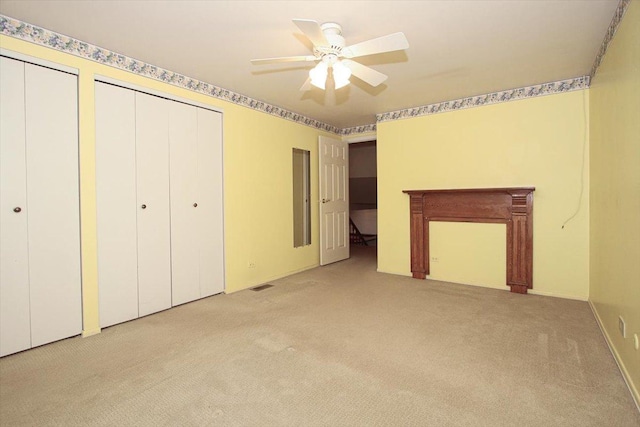 unfurnished bedroom featuring ceiling fan, light colored carpet, and multiple closets