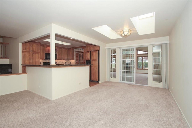 kitchen with light colored carpet, kitchen peninsula, french doors, and a skylight