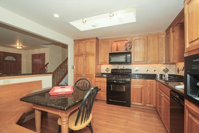 kitchen with dark stone countertops, decorative backsplash, black appliances, and light wood-type flooring