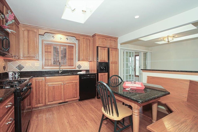 kitchen with black appliances, sink, a skylight, tasteful backsplash, and light hardwood / wood-style floors