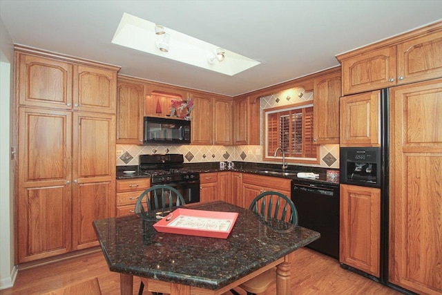 kitchen featuring decorative backsplash, a skylight, sink, black appliances, and light hardwood / wood-style floors