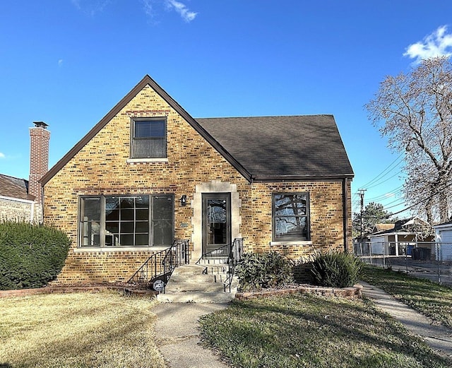 view of front of home with a shingled roof, brick siding, and fence