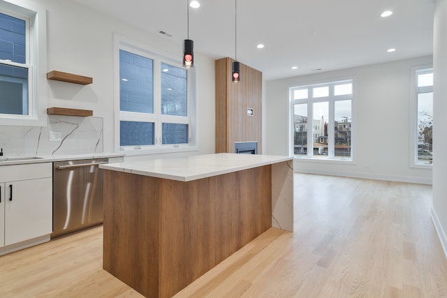 kitchen featuring white cabinets, dishwasher, a kitchen island, and a wealth of natural light