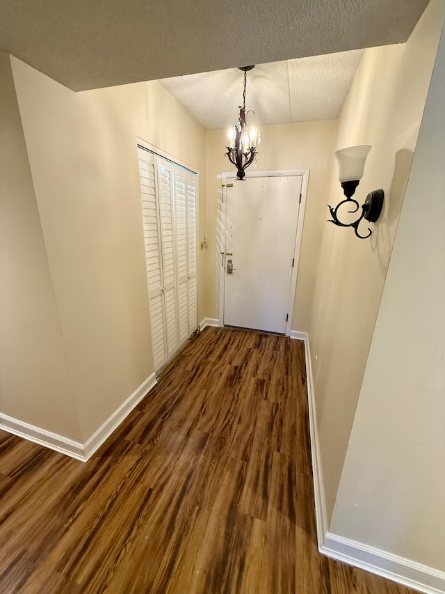 doorway to outside featuring a textured ceiling, dark hardwood / wood-style flooring, and a notable chandelier