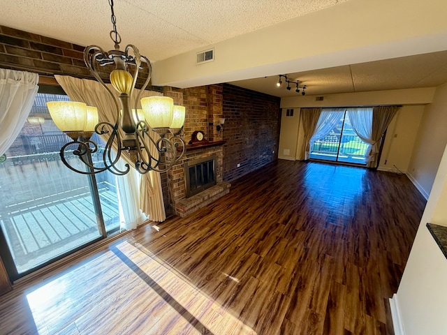 unfurnished living room with hardwood / wood-style floors, a brick fireplace, a textured ceiling, a notable chandelier, and brick wall