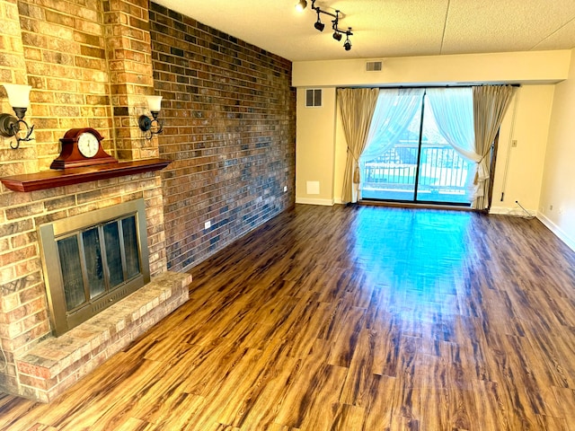 unfurnished living room with a brick fireplace, brick wall, a textured ceiling, and hardwood / wood-style flooring