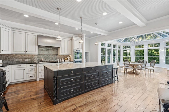 kitchen with beam ceiling, a kitchen island with sink, hanging light fixtures, and custom range hood