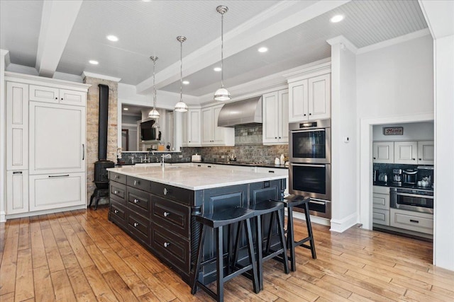 kitchen featuring wall chimney exhaust hood, backsplash, light hardwood / wood-style floors, decorative light fixtures, and white cabinets