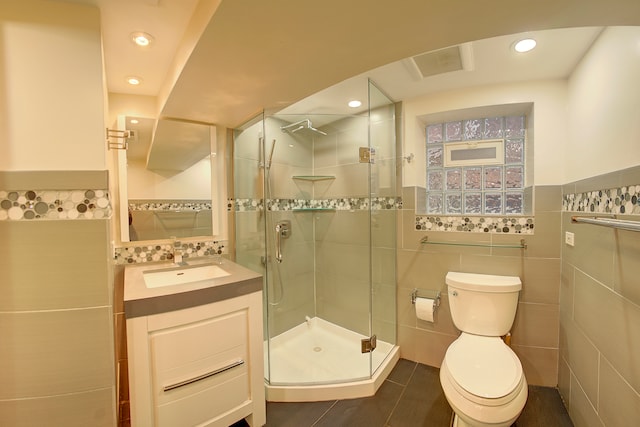 bathroom featuring vanity, toilet, a shower with door, and tile walls