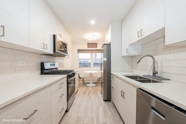 kitchen with white cabinets, sink, light wood-type flooring, appliances with stainless steel finishes, and tasteful backsplash