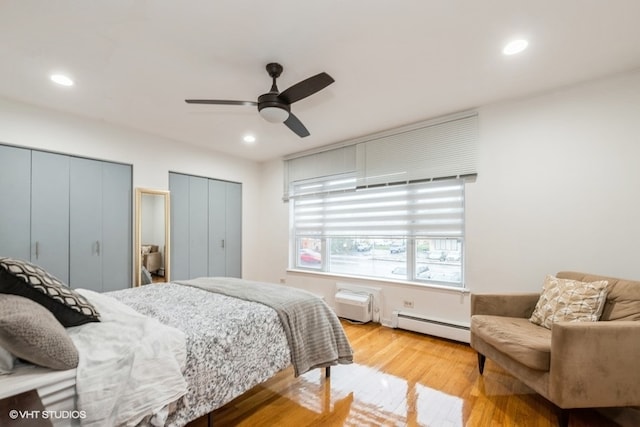 bedroom with ceiling fan, two closets, light wood-type flooring, and a baseboard heating unit