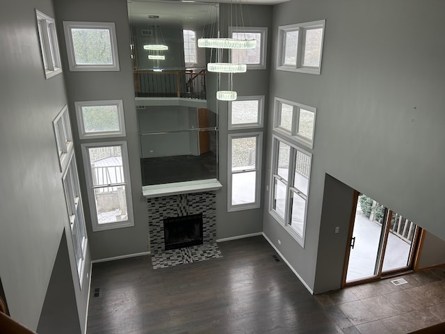 unfurnished living room featuring dark wood-type flooring, a notable chandelier, a healthy amount of sunlight, and a tiled fireplace