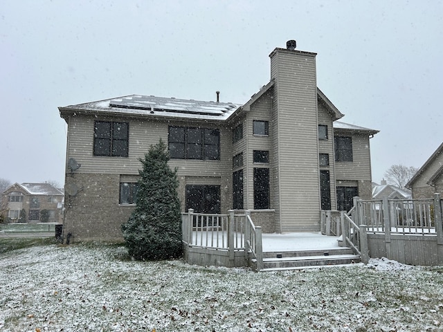 snow covered house featuring a wooden deck and solar panels