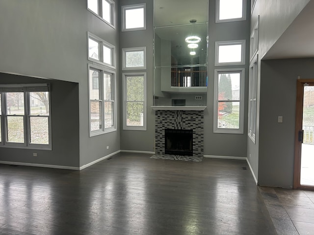 unfurnished living room featuring a towering ceiling, a healthy amount of sunlight, and a tiled fireplace