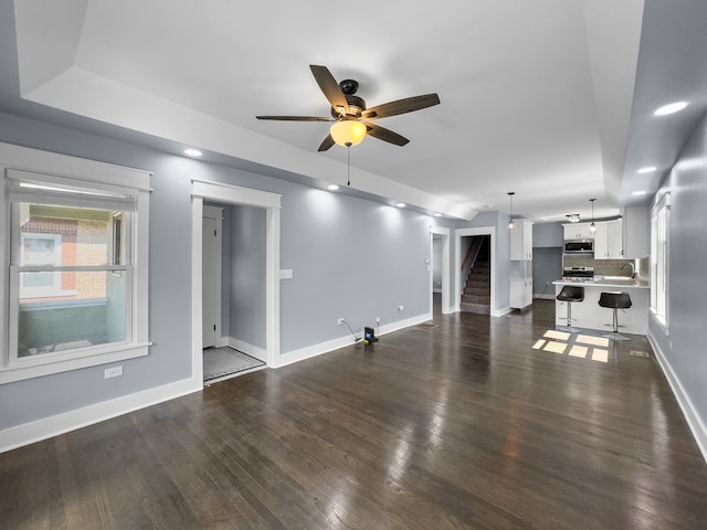 unfurnished living room featuring ceiling fan, sink, and dark wood-type flooring