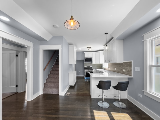 kitchen featuring kitchen peninsula, appliances with stainless steel finishes, tasteful backsplash, dark hardwood / wood-style floors, and white cabinetry