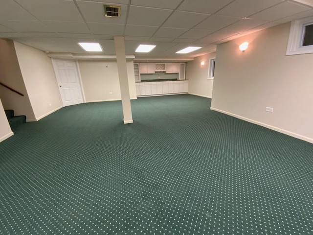 basement with a paneled ceiling and dark carpet