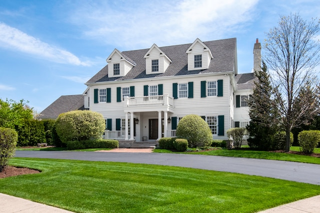 colonial house featuring a balcony and a front yard