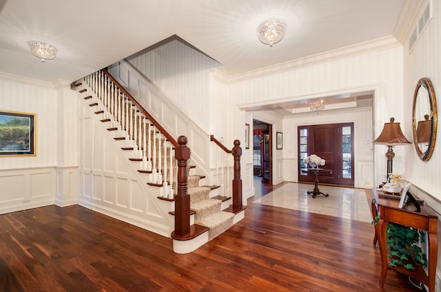 foyer entrance with a chandelier, dark wood-type flooring, and ornamental molding