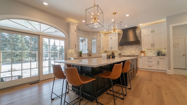 kitchen featuring pendant lighting, light hardwood / wood-style flooring, white cabinetry, custom range hood, and a kitchen island