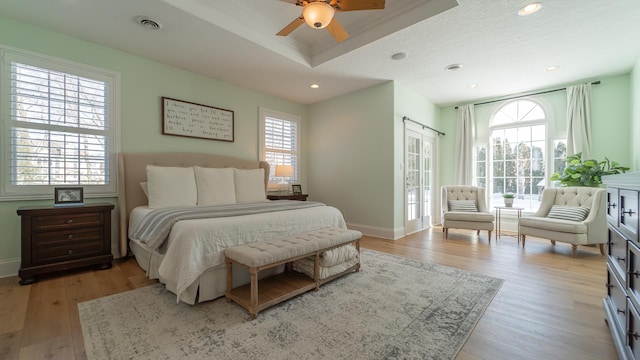 bedroom featuring a tray ceiling, light hardwood / wood-style floors, and multiple windows