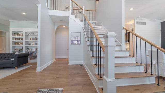 stairs featuring a high ceiling, wood-type flooring, and crown molding