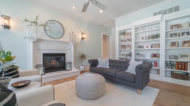 living room with hardwood / wood-style flooring, built in features, ornamental molding, and ceiling fan