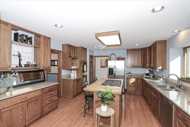 kitchen featuring sink, light wood-type flooring, light stone counters, a center island, and stainless steel appliances