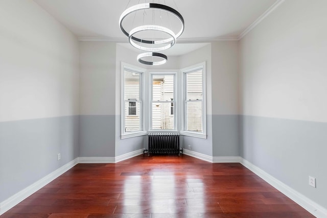 empty room featuring radiator, dark hardwood / wood-style flooring, ornamental molding, and a notable chandelier