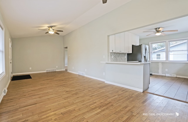 kitchen featuring kitchen peninsula, stainless steel refrigerator with ice dispenser, light wood-type flooring, backsplash, and white cabinetry