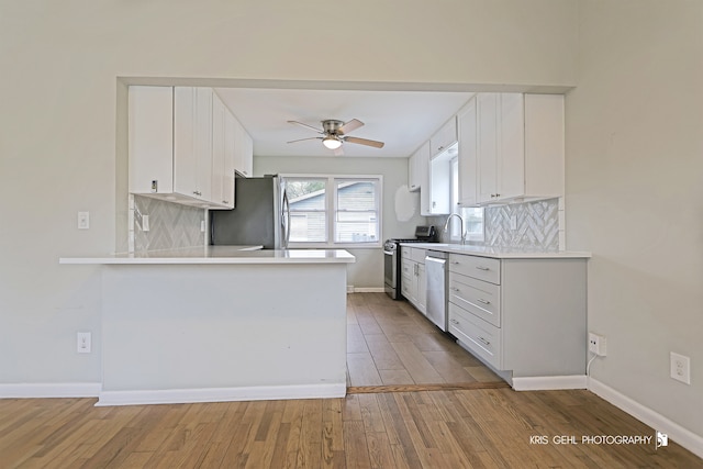 kitchen featuring tasteful backsplash, kitchen peninsula, light hardwood / wood-style floors, white cabinets, and appliances with stainless steel finishes