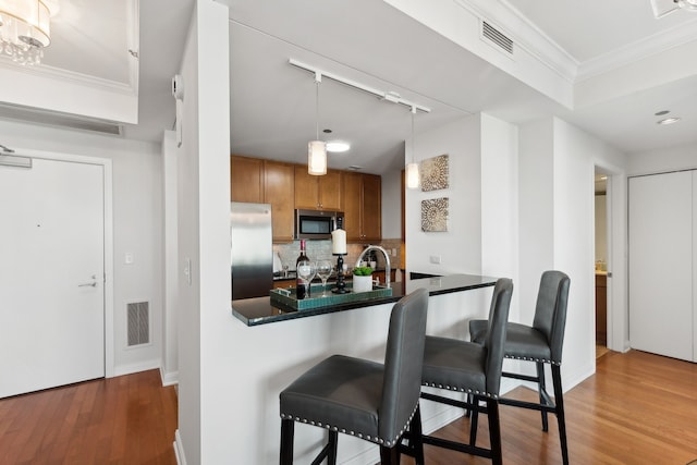 kitchen with tasteful backsplash, stainless steel appliances, crown molding, wood-type flooring, and decorative light fixtures