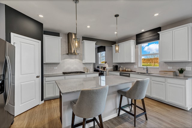 kitchen with stainless steel appliances, wall chimney range hood, decorative light fixtures, white cabinets, and a center island