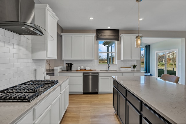 kitchen with white cabinets, decorative light fixtures, wall chimney range hood, and a wealth of natural light