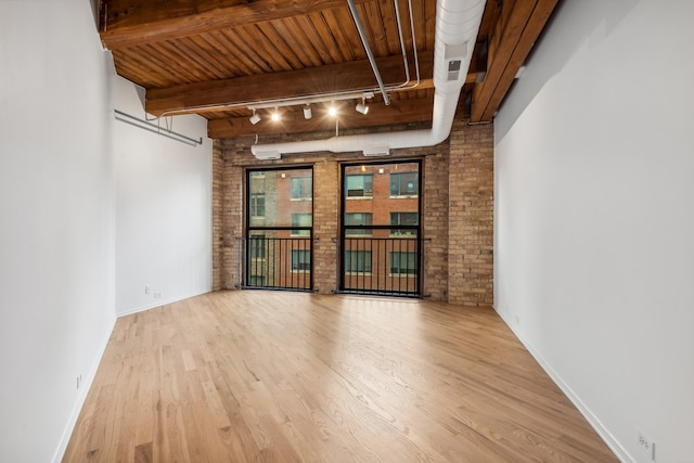 unfurnished room featuring beam ceiling, brick wall, wood-type flooring, and track lighting