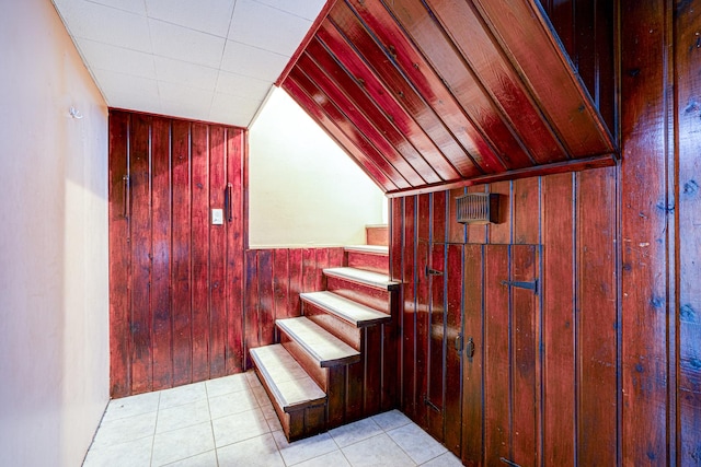 stairs with tile patterned floors, wooden walls, and lofted ceiling